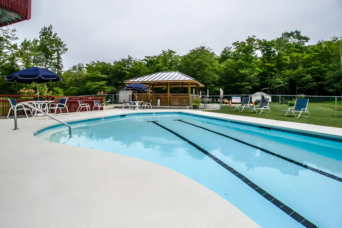A tranquil outdoor swimming pool surrounded by lounge chairs and a gazebo, set amidst greenery. The clear water, ample seating, and shaded area create an inviting scene for relaxation and recreation.