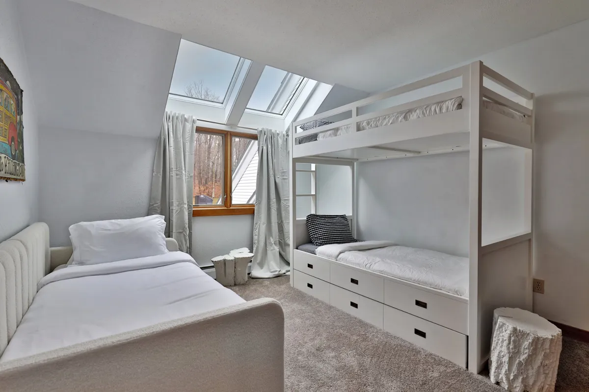 A playful, inviting bedroom featuring a sturdy bunk bed and a separate single bed, with a large window providing natural light and a whimsical, relaxed vibe. The room is ideal for children or agile guests, in line with the safety advisory for bunk access.