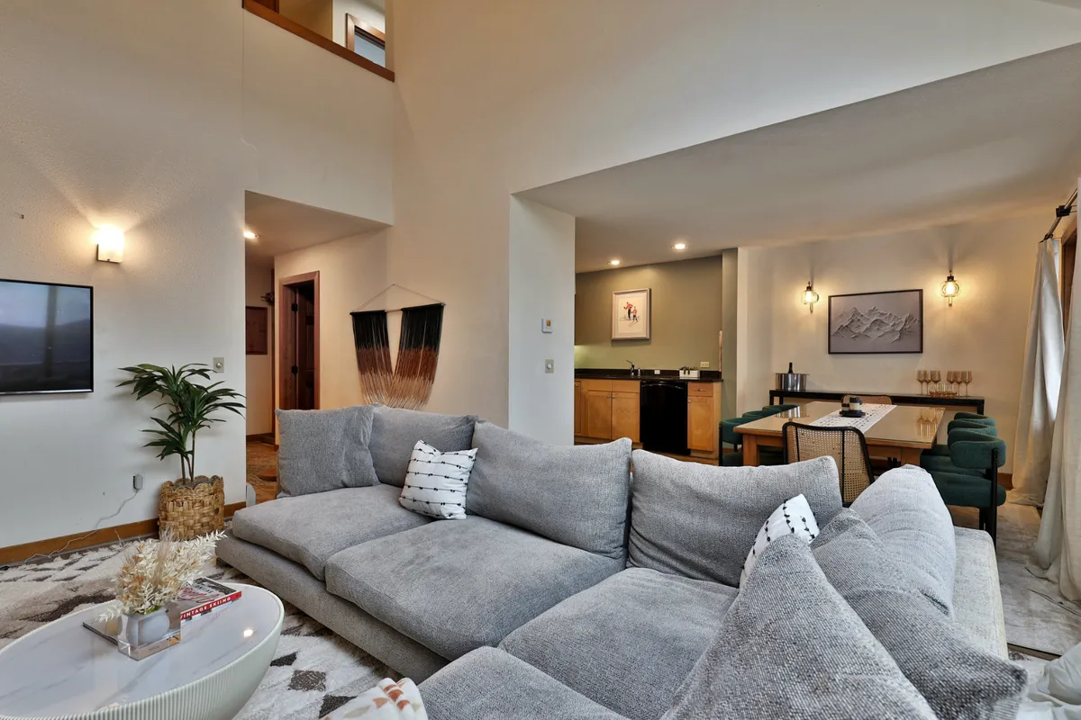 A wide-angle view of an open-concept living and dining space, where a comfortable sofa faces a dining table. The kitchen area is visible in the background, blending seamlessly with the social areas. Soft lighting and wall art add to the inviting atmosphere, ideal for family meals or group game nights.