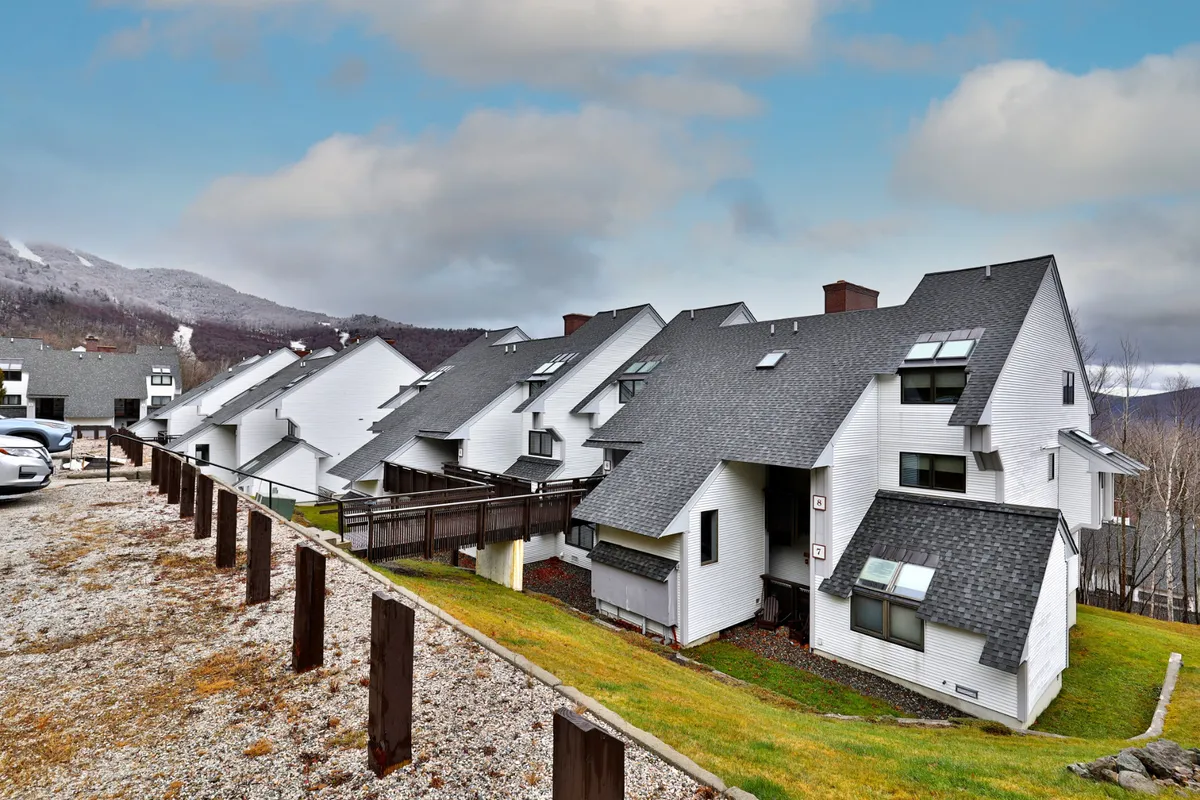 A serene exterior view showcasing the arrangement of the buildings, sloped roofs, and surrounding mountain landscape at sunset. The setting evokes a sense of relaxation and connection to the area's natural beauty, hinting at the lively attractions nearby.