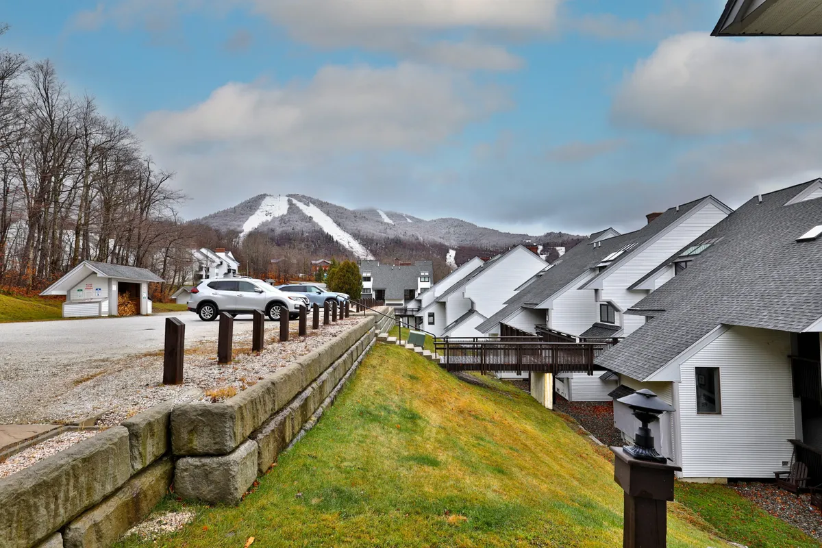 A stunning winter exterior scene with snow-covered mountains in the background, residential buildings in the midground, and a parking area in the foreground. The landscape evokes the excitement of ski season and winter sports, while the serene atmosphere hints at peaceful moments after a day of adventure.