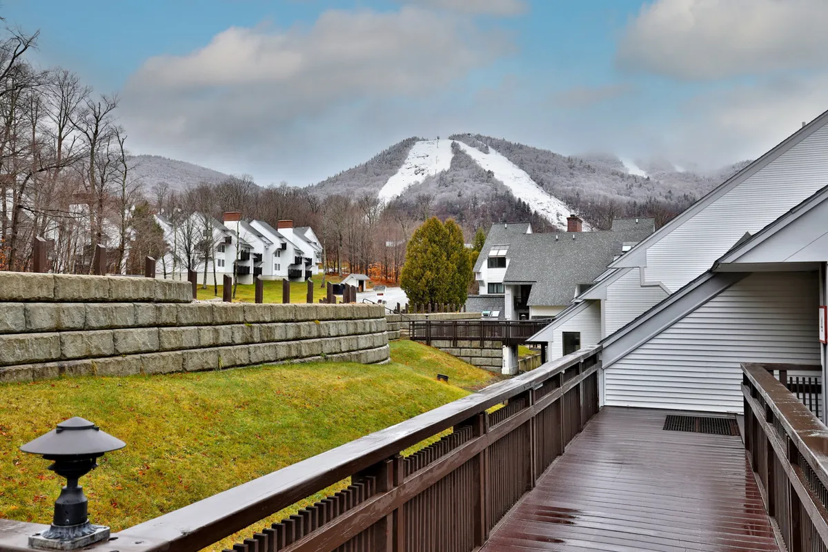 This exterior image showcases mountain slopes, a walkway leading toward residential buildings, and the natural landscape. The snow-dusted terrain and visible ski slopes immediately convey the resort’s direct mountain access and ski-friendly setting.