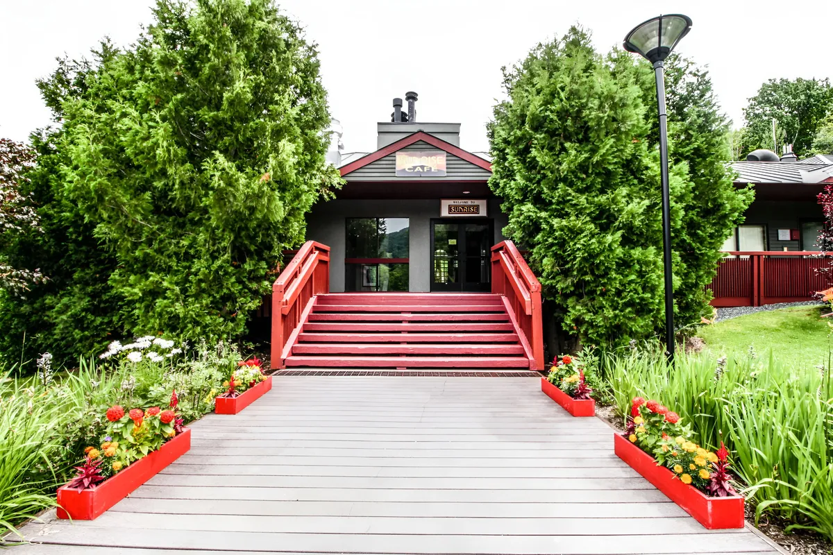 This exterior shot captures the front entryway of the property, highlighting a red staircase flanked by green hedges, vibrant flower beds, and a cheerful lamp post leading to the front door. The scene evokes a welcoming, family-friendly atmosphere and emphasizes safe, easy access to the home.
