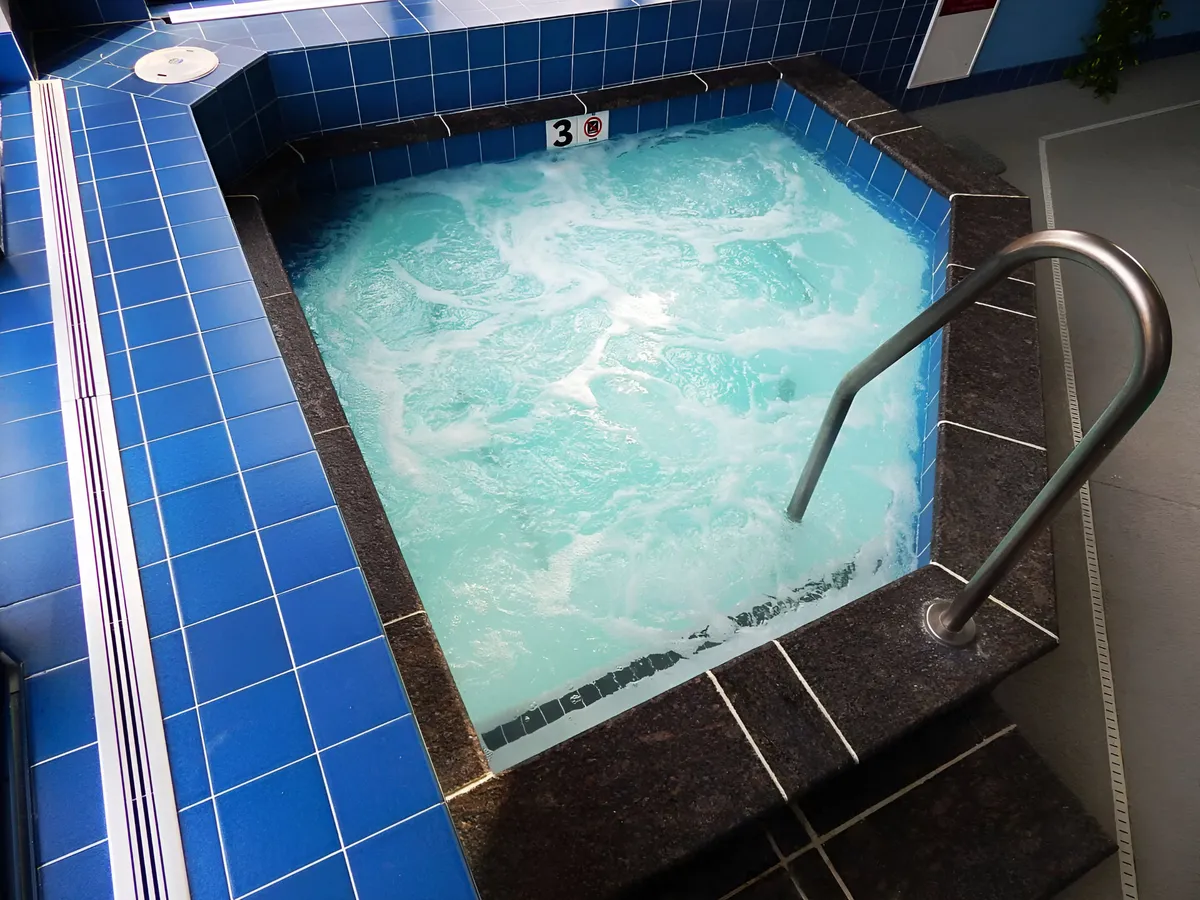 A serene indoor jacuzzi with blue tile accents and a stainless steel railing. The setup suggests a soothing space intended for relaxation and wellness.