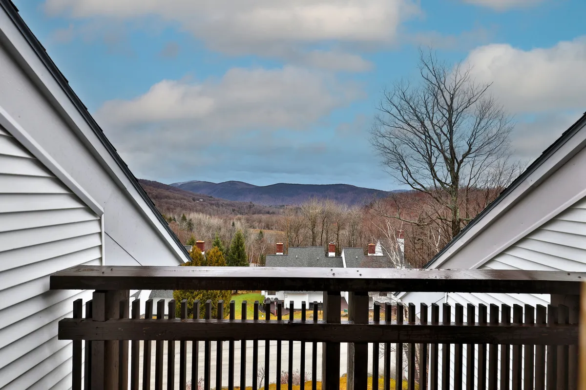 An elevated view from a wooden balcony reveals a sweeping mountain range under a cloudy sky. The image radiates the tranquility of the natural environment and hints at activities like morning coffee or watching the sunrise after a day of skiing.