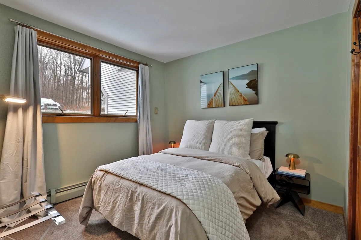 A serene bedroom with a comfortable bed topped with soft linens, artwork above the headboard, and a large window letting in natural morning light. The mood is tranquil and restful, perfect for a peaceful night's sleep.