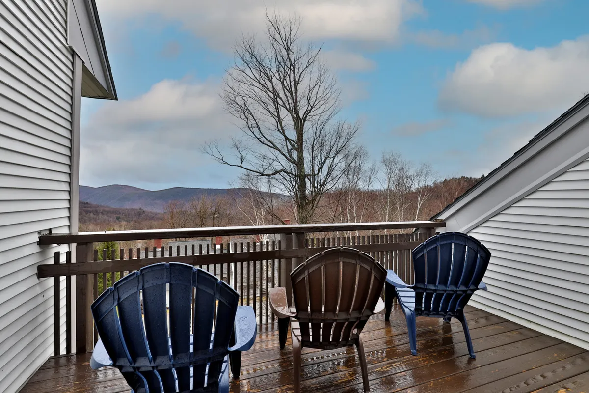 A peaceful deck scene featuring Adirondack chairs facing striking mountain views. Bare trees suggest seasonal transitions, while the expansive vista captures Vermont's natural beauty and the inviting outdoors—perfect for relaxation after a day of adventure.