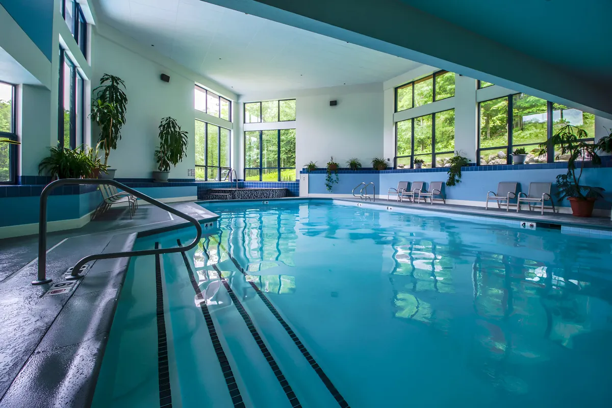 An inviting indoor pool area with large windows, abundant natural light, potted plants, and a jacuzzi area. The scene evokes relaxation, wellness, and a space to unwind after outdoor adventures.