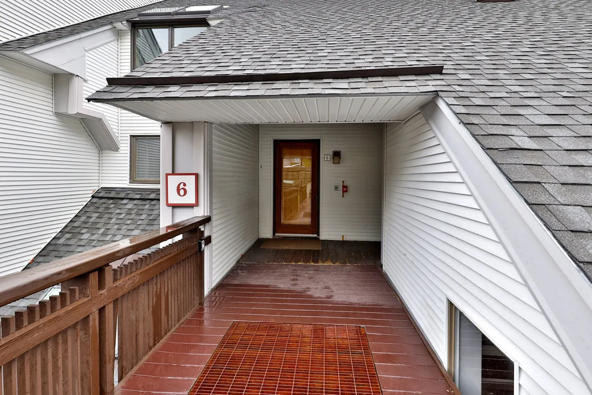 The exterior entrance to the condo, featuring a welcoming door, number 6 sign, and a wooden railing. The scene is calm and inviting, emphasizing easy access and the welcoming atmosphere guests experience upon arrival.